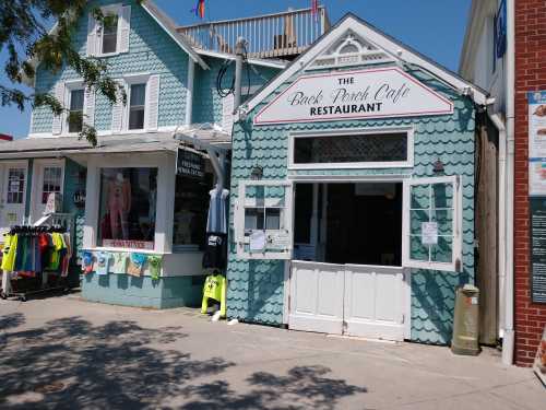 A turquoise building with a sign reading "The Back Porch Cafe Restaurant," featuring outdoor seating and nearby shops.