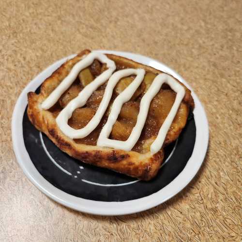 A pastry topped with apple filling and drizzled with white icing on a black plate.