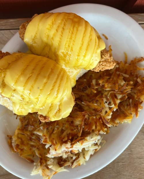 A plate featuring two fried chicken sandwiches topped with melted cheese, alongside a serving of crispy hash browns.