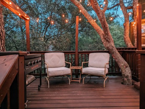 Cozy deck with two chairs, a small table, and string lights hanging from trees, creating a warm evening atmosphere.