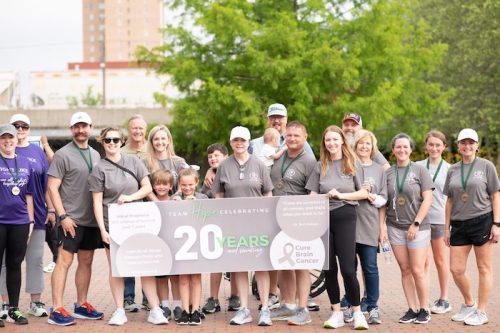 A group of people in gray shirts holding a banner celebrating 20 years of Team Hope and Cure Brain Cancer.