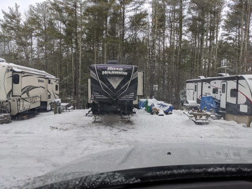 A snowy campsite with several RVs parked among trees, featuring a prominent "Road Warrior" RV in the center.