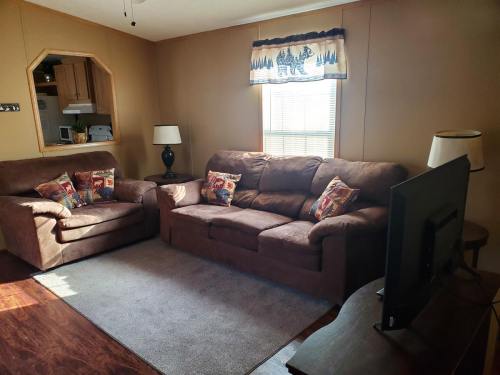 Cozy living room with brown sofas, decorative pillows, a TV, and a window with light curtains.