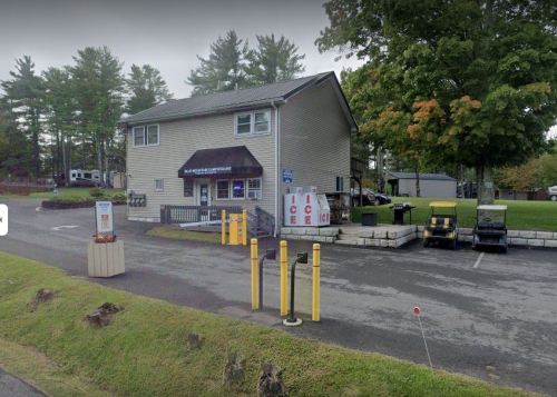 A two-story building with a sign, surrounded by trees, and a parking area with golf carts and an ice stand.