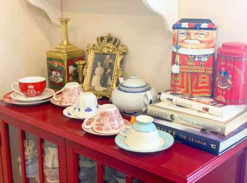 A red cabinet displays vintage teacups, a teapot, books, and decorative tins, creating a charming, nostalgic scene.