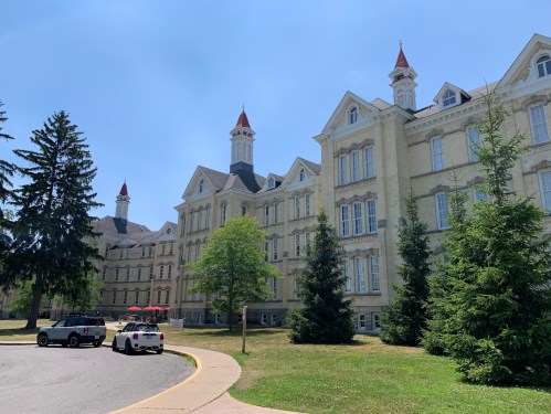 Historic building with pointed towers, surrounded by trees and a clear blue sky, featuring a curved pathway in the foreground.