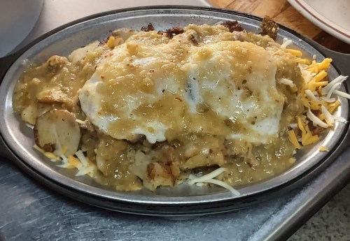 A sizzling platter of cheesy, saucy breakfast dish with eggs, potatoes, and toppings, served hot.