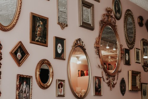 A wall adorned with various ornate mirrors and framed artwork in a cozy, vintage setting.