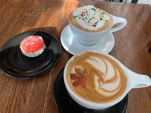 A cozy café scene featuring two cups of coffee with whipped cream and a festive cupcake on a wooden table.