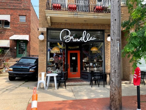 A storefront with the sign "Brewella's," featuring outdoor seating and a black vehicle parked nearby.
