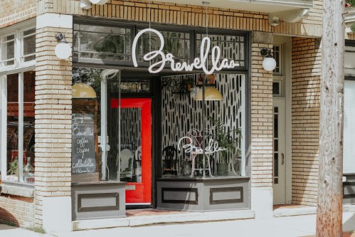 A cozy café storefront with large windows, a red door, and stylish signage reading "Brewella."