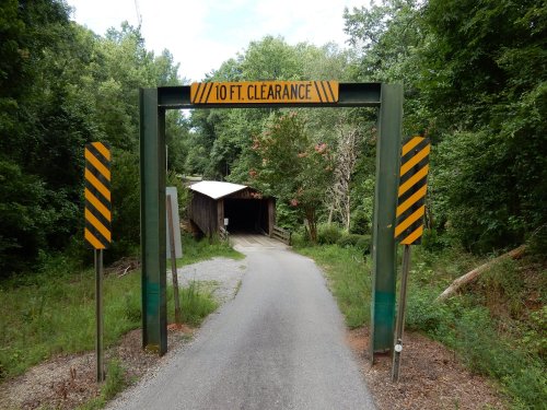 A road leads to a covered bridge, marked with a sign indicating a 10 ft. clearance, surrounded by trees.