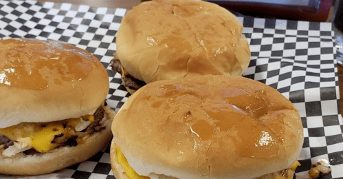 Three cheeseburgers on a checkered paper plate, featuring melted cheese and shiny, toasted buns.