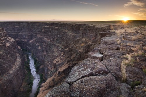 A scenic view of a deep canyon at sunrise, with a river winding through the rocky landscape.