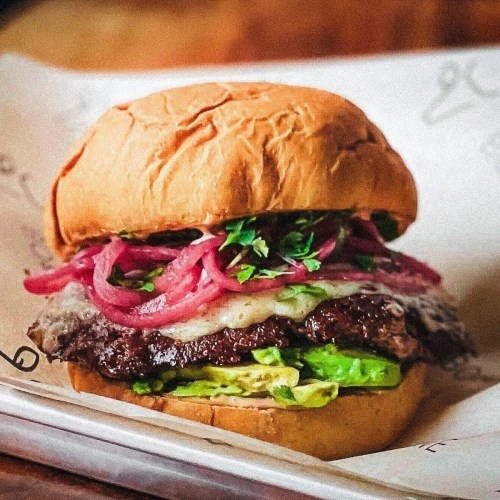 A delicious burger with a juicy patty, melted cheese, avocado, pickled onions, and fresh herbs on a soft bun.