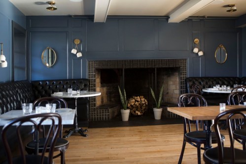 Cozy restaurant interior featuring dark blue walls, a fireplace, wooden floors, and elegant seating arrangements.