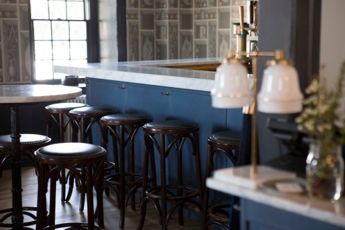 A stylish bar area featuring a marble countertop, wooden stools, and elegant lighting in a cozy setting.
