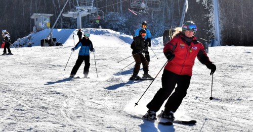 Skiers navigate a snowy slope with a ski lift in the background on a sunny day.