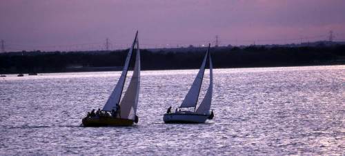 Two sailboats glide across a shimmering body of water at sunset, with a purple sky in the background.