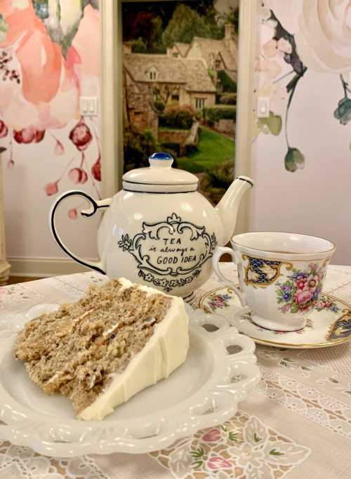 A teapot and a cup beside a slice of cake on a decorative plate, set against a floral backdrop.