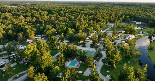 Aerial view of a lush campground with RVs, a swimming pool, and winding roads surrounded by dense trees.