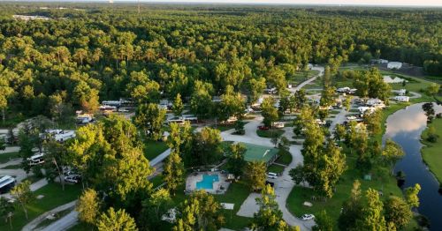 Aerial view of a lush campground with RVs, trees, a pool, and winding roads surrounded by greenery.
