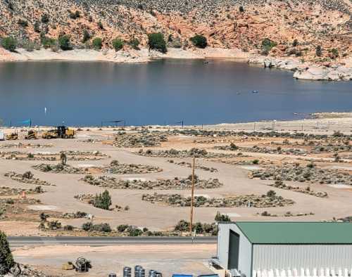 A scenic view of a lake surrounded by rocky terrain, with construction equipment and sparse vegetation in the foreground.