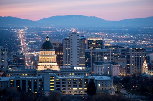 A panoramic view of a city skyline at dusk, featuring a prominent dome building and distant mountains.