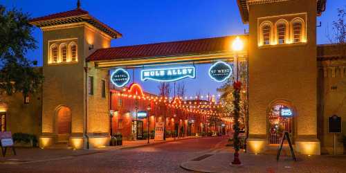 Entrance to Mule Alley at dusk, featuring illuminated signs and charming architecture with string lights.