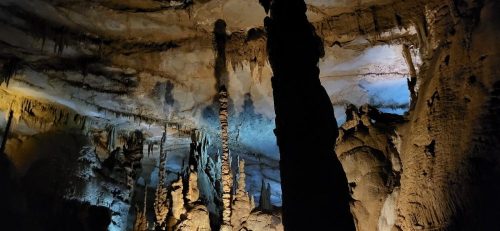 A stunning cave interior featuring tall stalagmites and stalactites illuminated by blue and warm lighting.