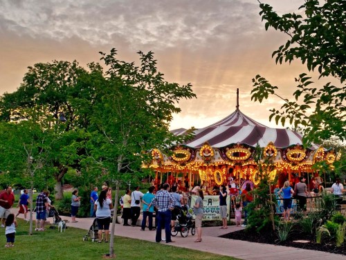 A vibrant carousel surrounded by people and trees, with a colorful sunset in the background.