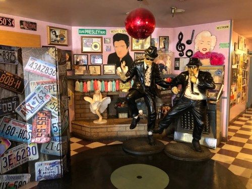 A colorful diner interior featuring statues of two musicians, vintage decor, and a disco ball.