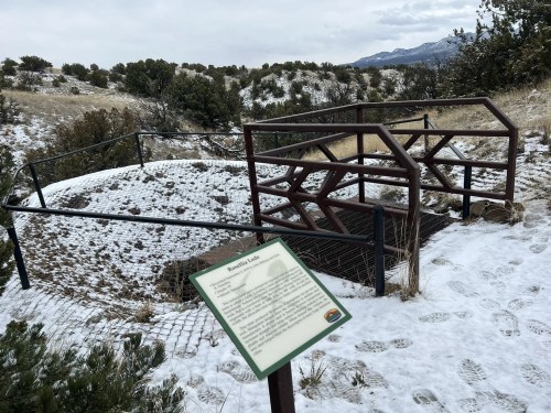 A snowy landscape featuring a fenced archaeological site and an informational sign about the area.