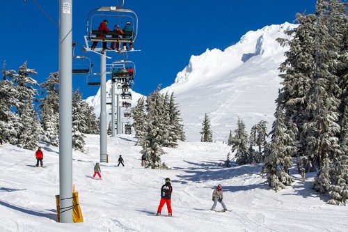 Skiers on a snowy slope with a ski lift in the background and trees under a clear blue sky.
