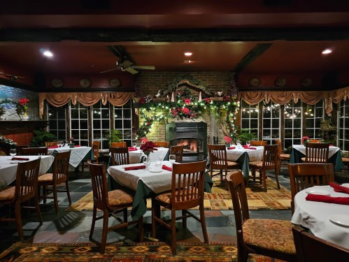 Cozy restaurant interior with tables set for dining, a fireplace, and festive holiday decorations.