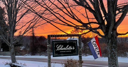 A restaurant sign reading "Charlotte's" with an "OPEN" flag, set against a vibrant sunset and snowy landscape.