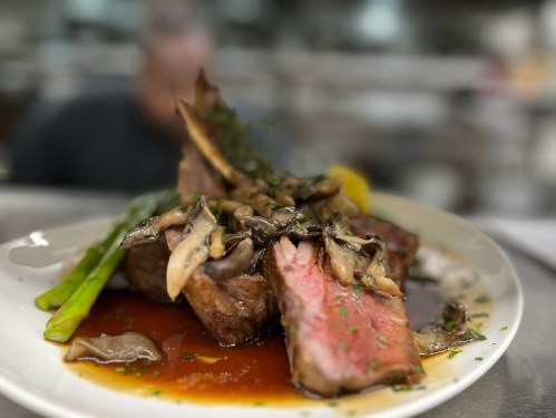 A plate of succulent steak topped with mushrooms and herbs, served with asparagus and a rich sauce.