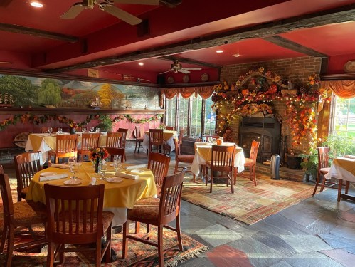 Cozy restaurant interior with wooden tables, colorful decor, and a fireplace adorned with autumn leaves.