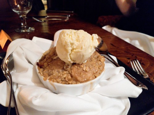 A warm dessert topped with a scoop of vanilla ice cream, served in a white dish on a napkin.