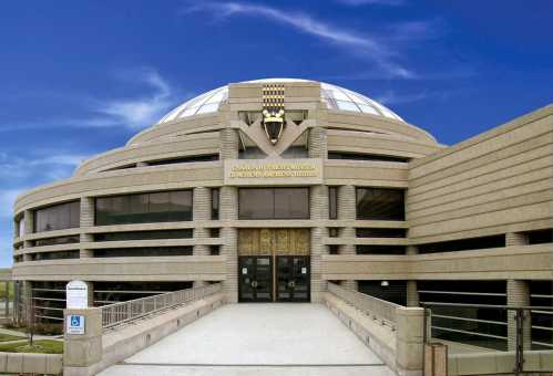 Exterior view of a modern museum building with a domed roof and decorative entrance, set against a blue sky.