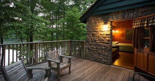 Cozy cabin deck with wooden chairs, overlooking trees and a lake, inviting relaxation in nature.