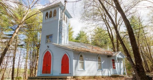 A charming blue church with red doors, surrounded by trees in a serene outdoor setting.