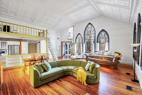 Bright, spacious living area with a green sectional sofa, wooden floors, and large arched windows. Cozy and inviting atmosphere.