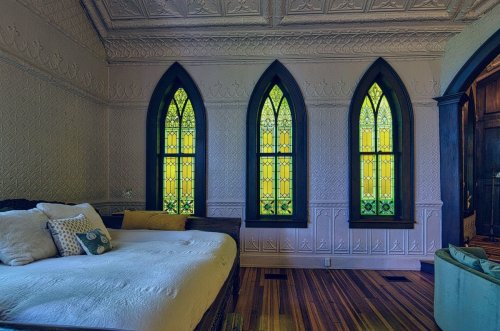 A cozy room featuring a bed and three tall, colorful stained glass windows with intricate designs.