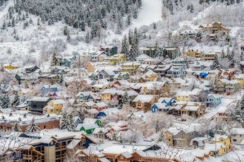 A picturesque snowy village with colorful houses nestled among trees, surrounded by a winter landscape.