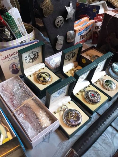 A collection of decorative pocket watches displayed in boxes, alongside various badges and items on a table.