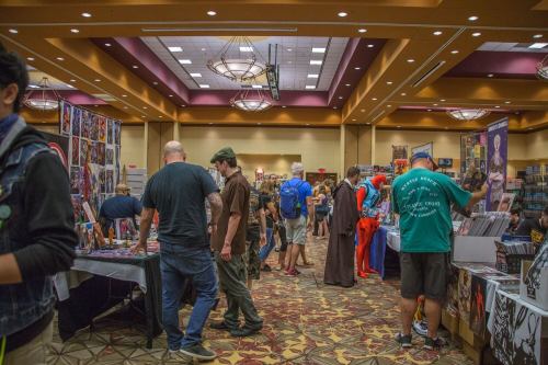 A bustling convention scene with vendors, attendees, and colorful displays of comics and merchandise.