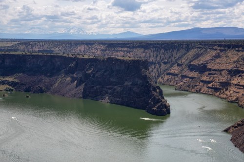 A scenic view of a green river winding through rocky cliffs, with mountains in the background under a cloudy sky.