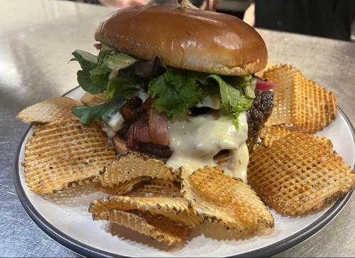 A juicy burger topped with lettuce, bacon, and sauce, served with crispy waffle fries on a plate.