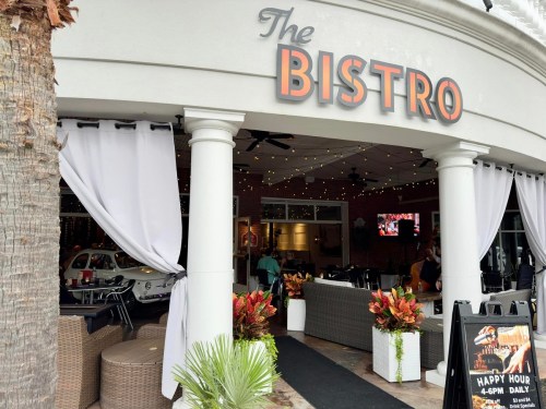 Entrance to The Bistro, featuring outdoor seating, plants, and a sign advertising happy hour.
